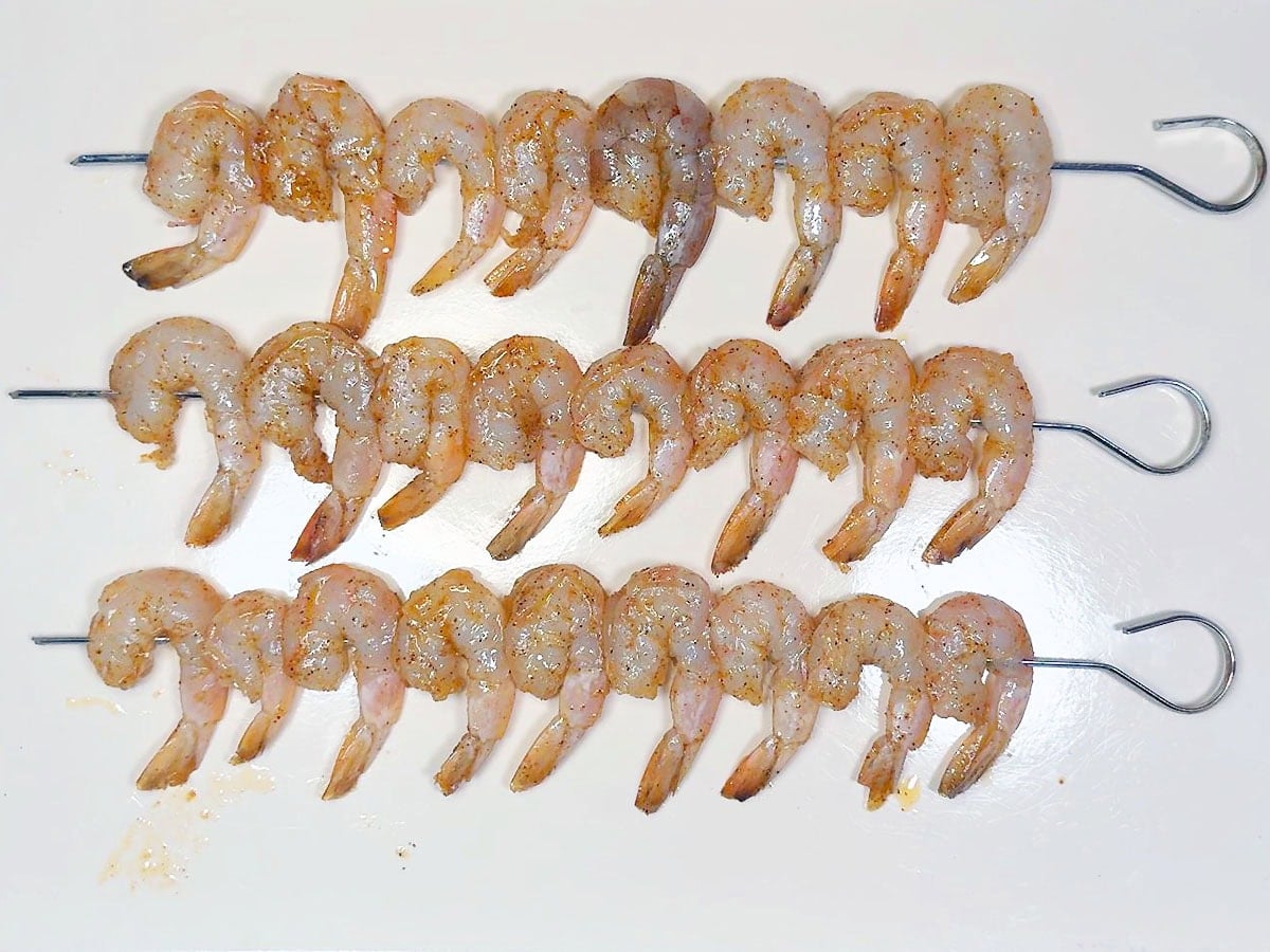 Seasoned raw shrimp threaded on metal skewers.