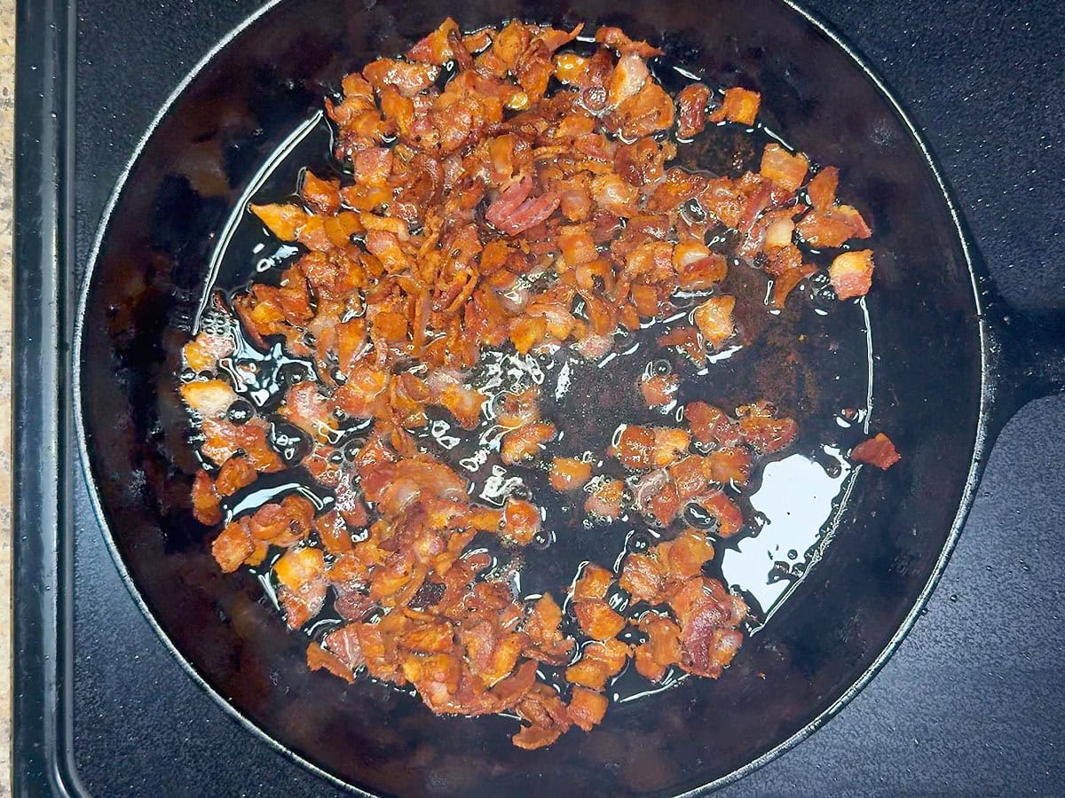 Cooking diced bacon pieces until crisp in a cast iron skillet.