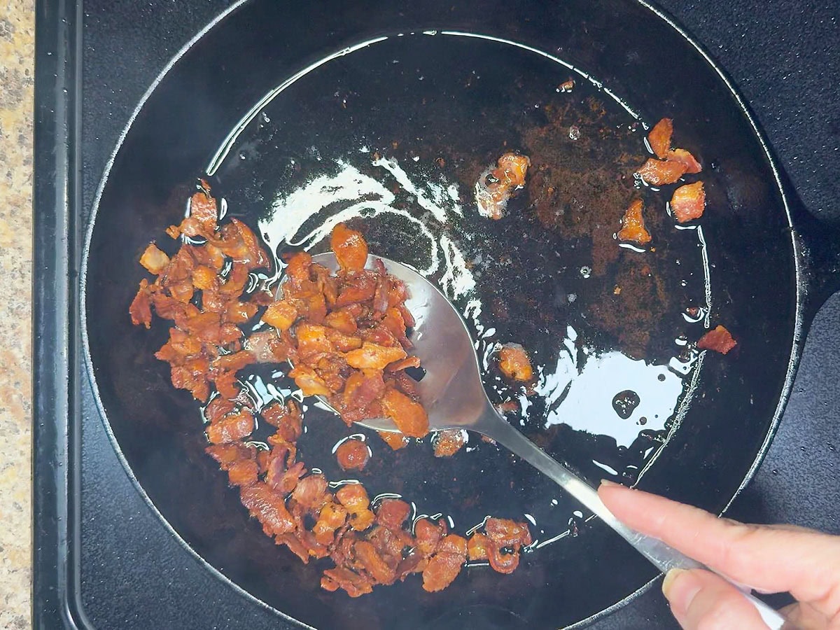 Removing the cooked bacon from the skillet with a slotted spoon and leaving behind the bacon grease.
