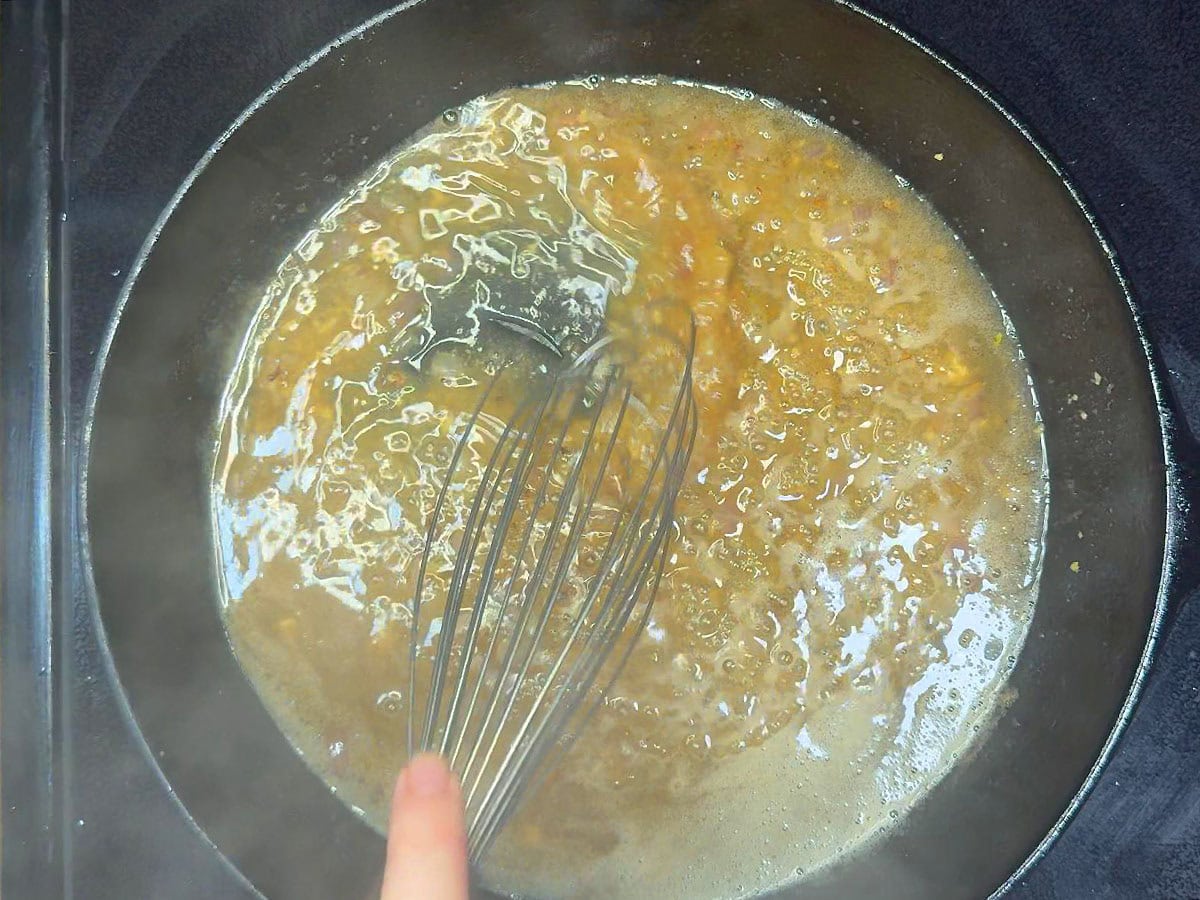 Whisking apple cider vinegar and dijon mustard into the bacon grease.