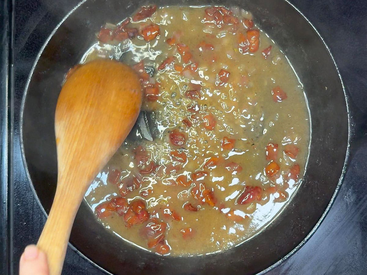 Stirring the cooked bacon back into the skillet with the hot bacon dressing.