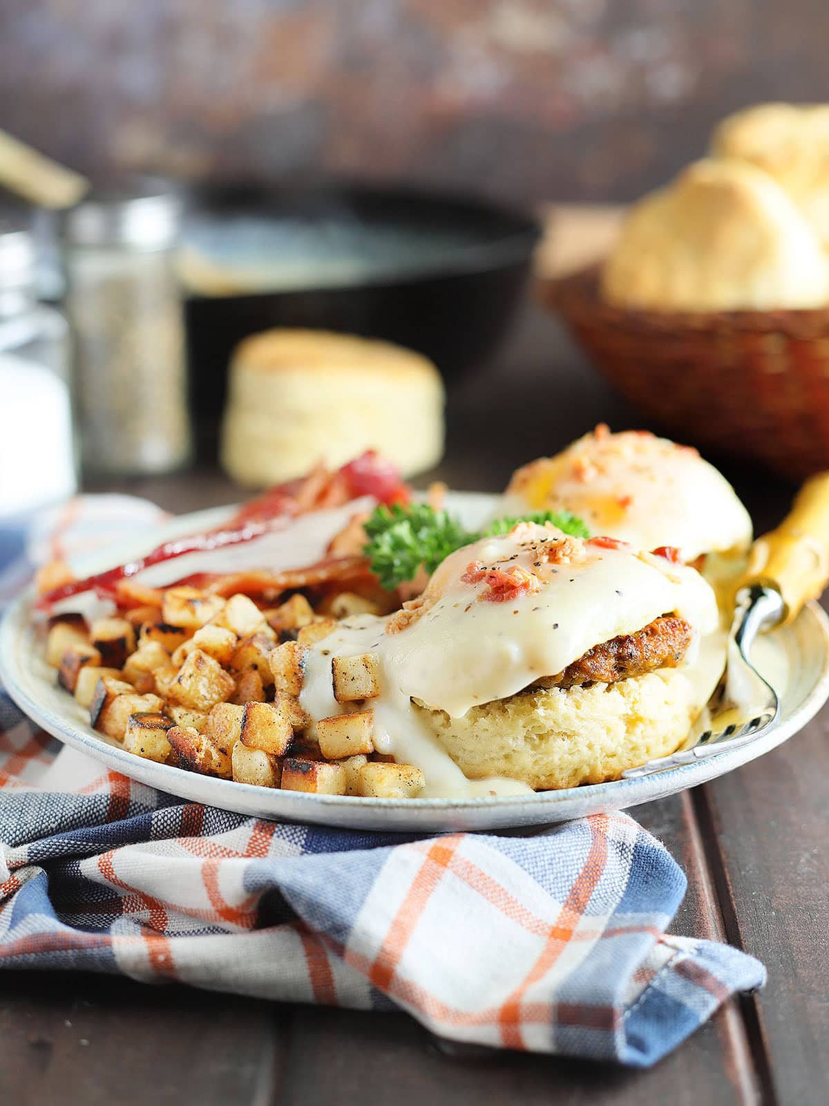Country eggs benedict on a plate with a side of hash brown potatoes and bacon.