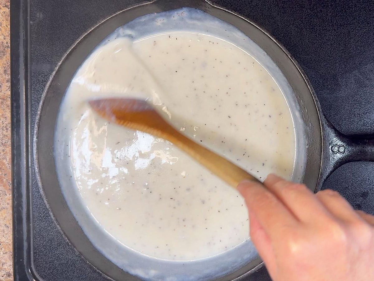 Stirring the cream gravy until thickened.