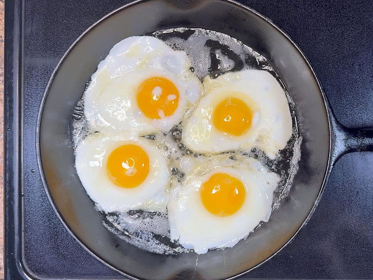 Frying four eggs in butter in a cast iron skillet.
