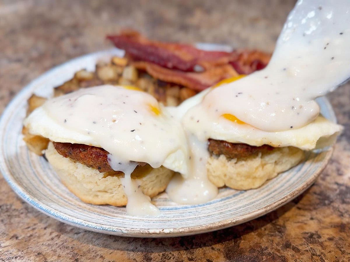 Pouring cream gravy over the eggs, patty sausage and biscuits.