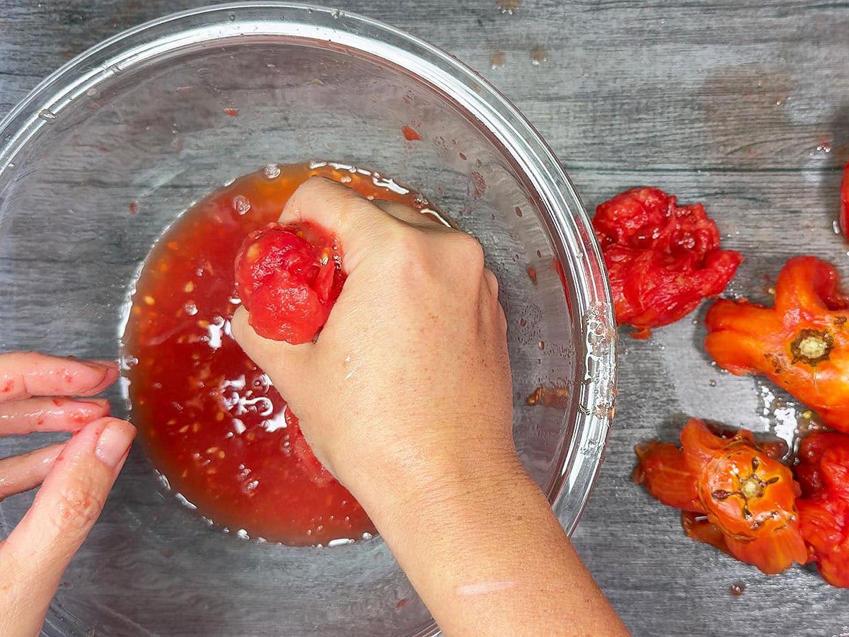 Squeezing a peeled tomato over a bowl to extract the juice.