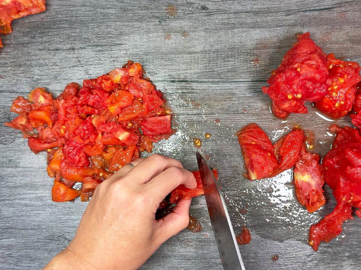 Cutting up peeled, cored and juiced tomatoes into smaller pieces.