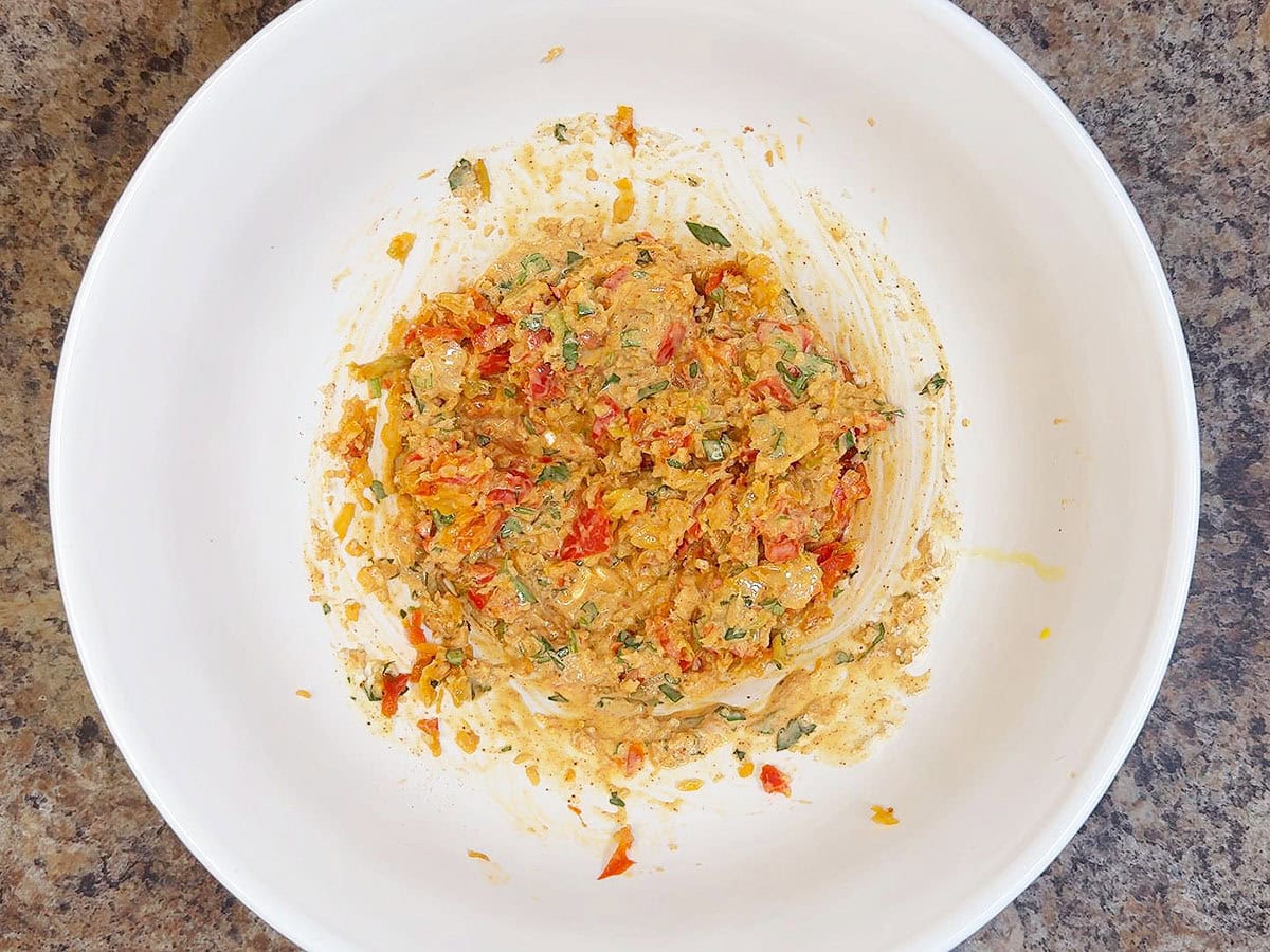 Egg, mayonnaise, Worcestershire sauce, Dijon mustard, paprika, parsley, cayenne pepper, and cooked vegetables mixed together in a mixing bowl.