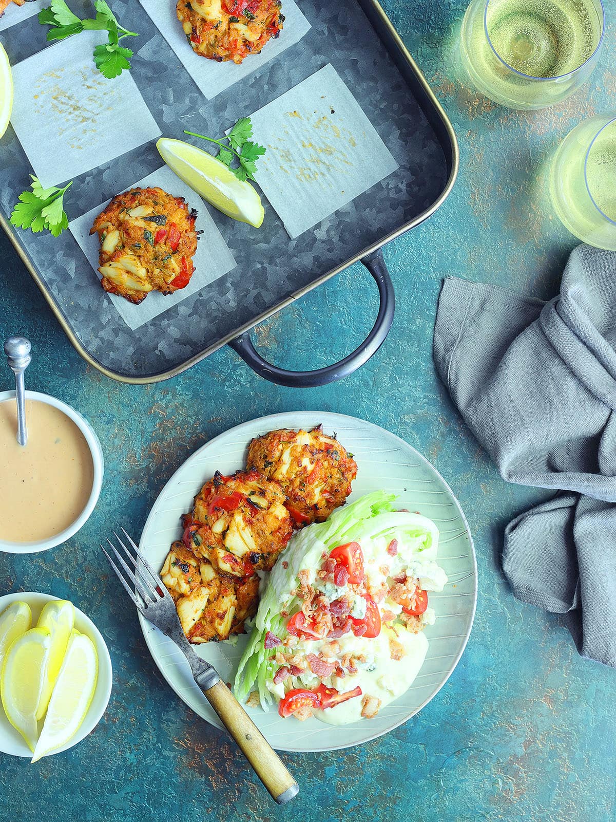 Three crab cakes on a plate with a wedge salad on the side.