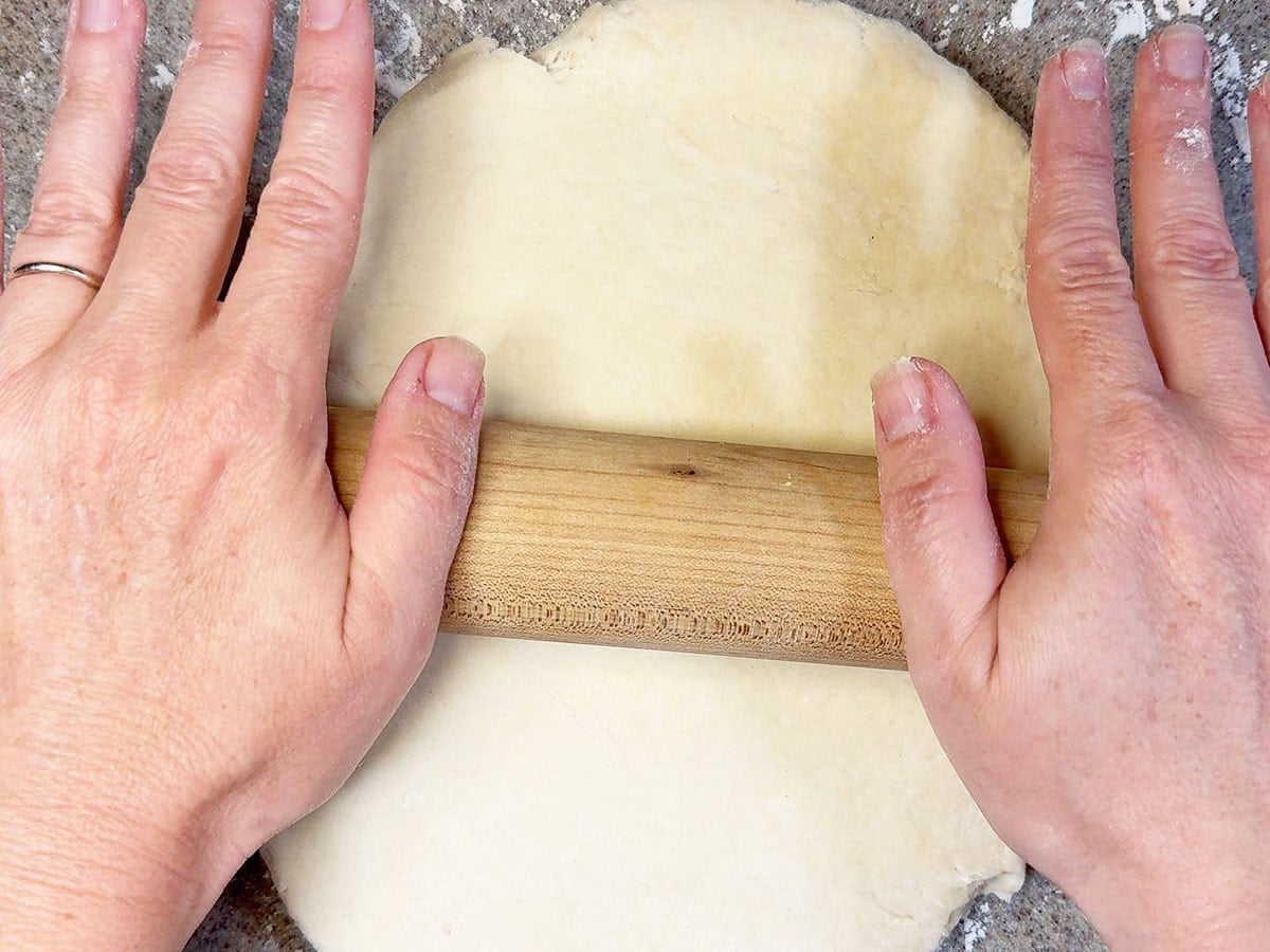 Using a rolling pin to roll out the biscuit dough on a lightly floured surface.