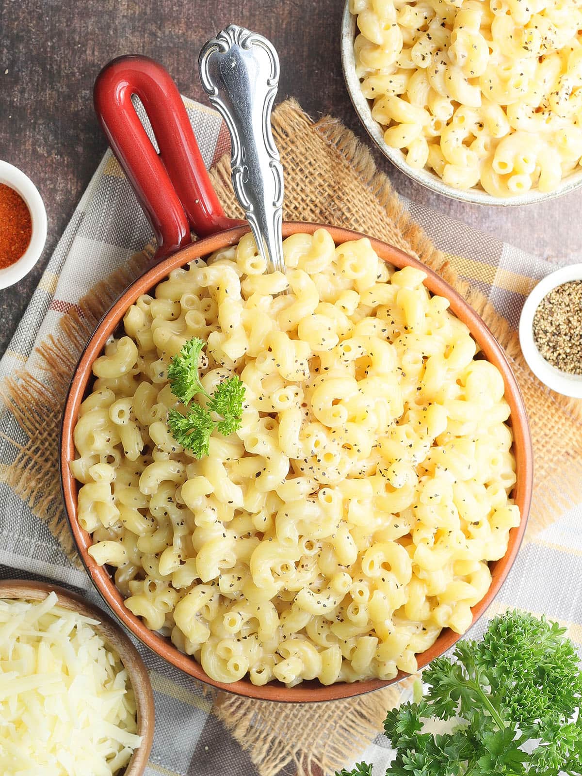 Bowl of creamy mac and cheese with a serving spoon and garnished with parsley and black pepper.