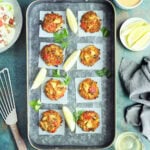 Oven baked crab cakes arranged on a metal serving tray with lemon wedges.