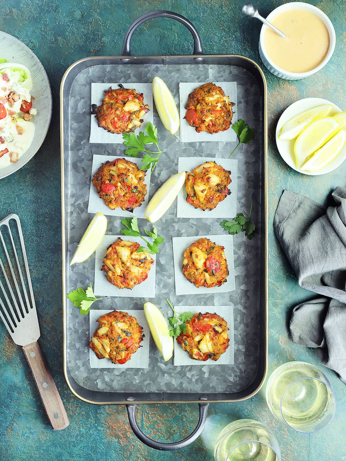 Oven baked crab cakes arranged on a metal serving tray with lemon wedges.