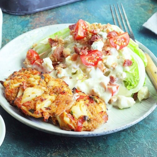 Three crab cakes on a plate with a wedge salad on the side.