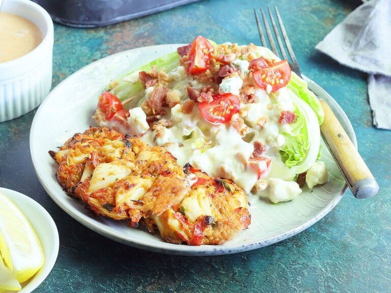 Three crab cakes on a plate with a wedge salad on the side.
