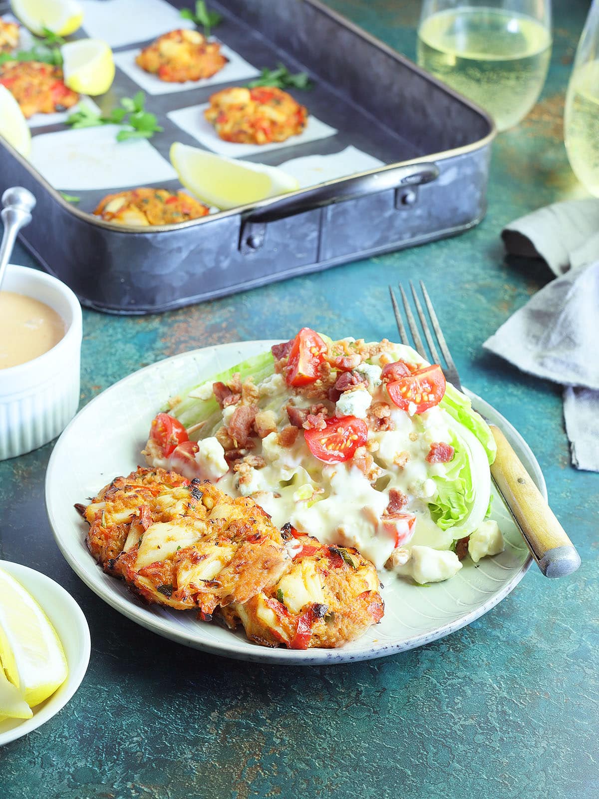Three crab cakes on a plate with a wedge salad on the side.