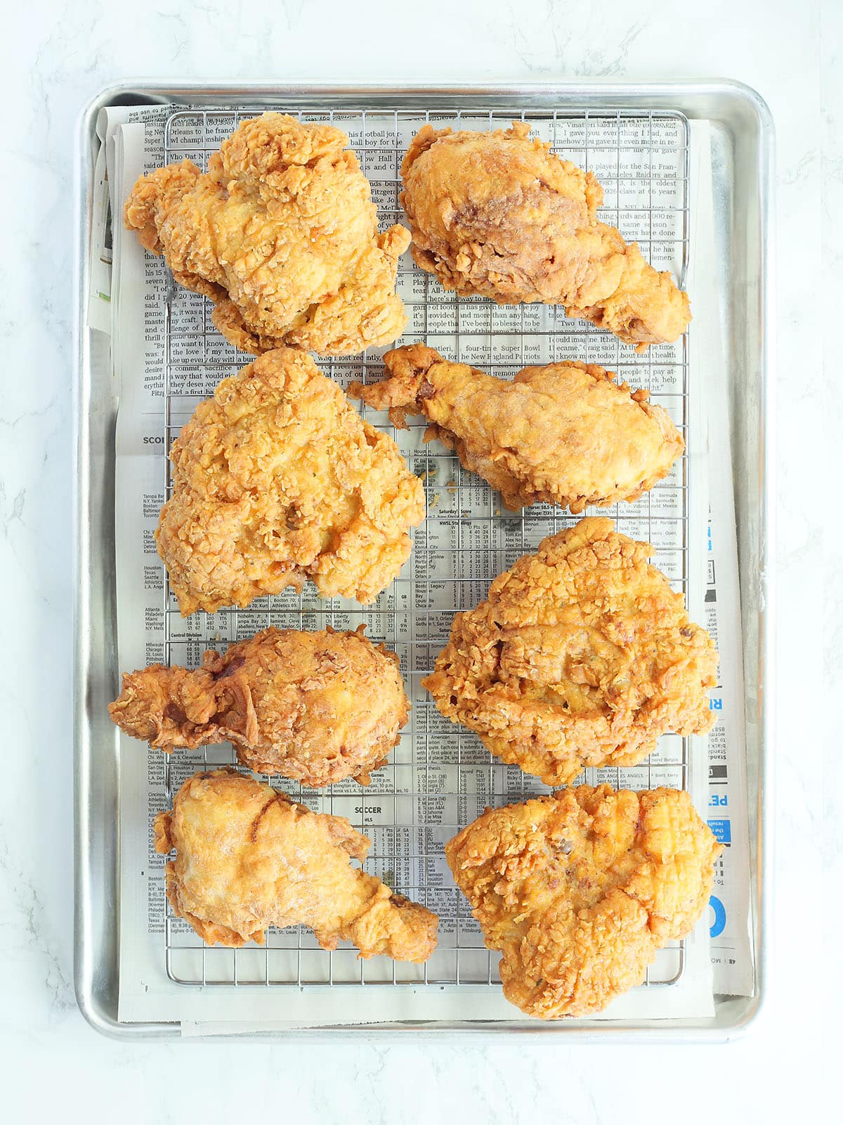 Fried chicken draining on a rack over a layer of paper towels.