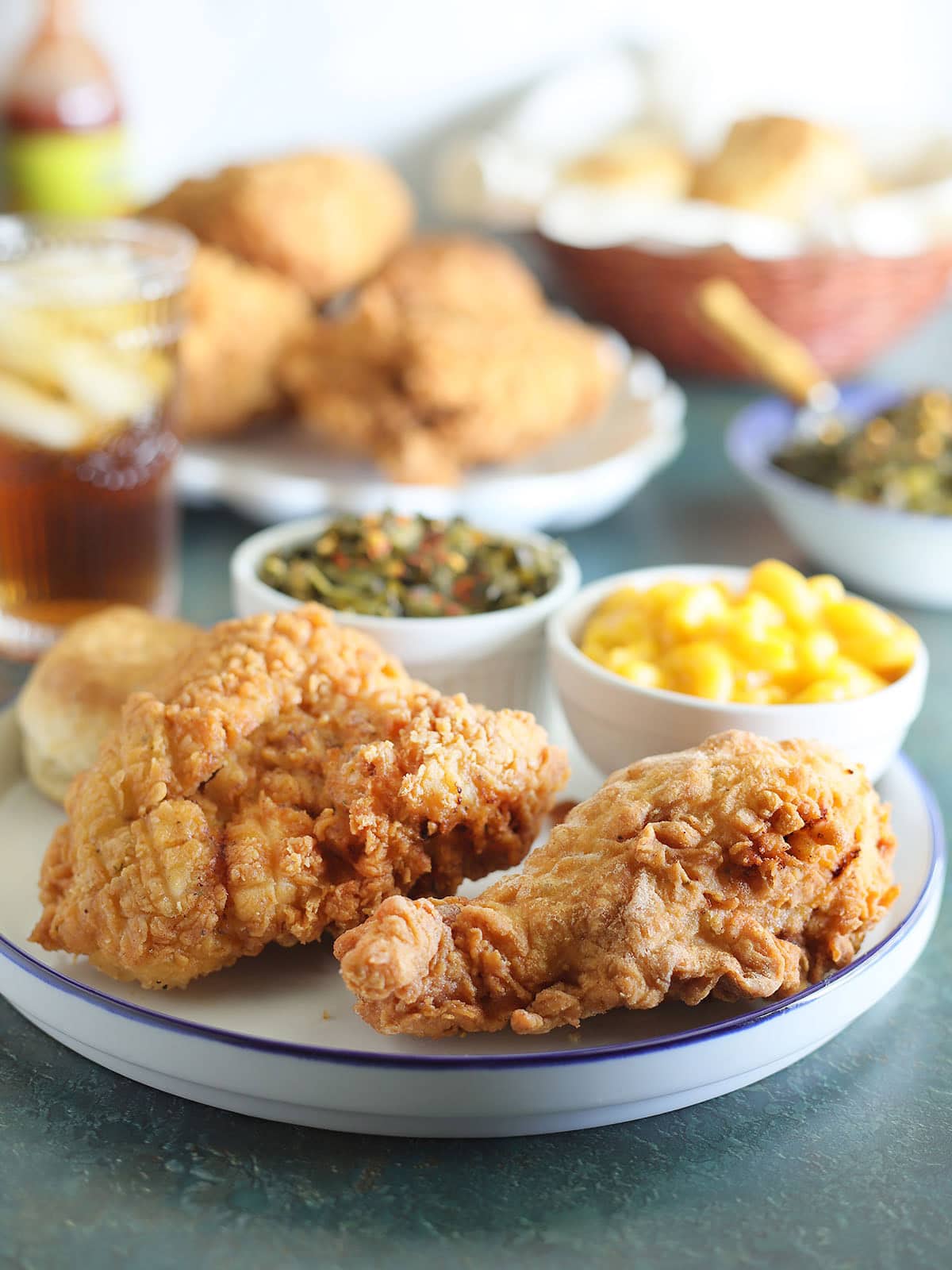 Two pieces of fried chicken on a plate with a dish of macaroni and cheese and collard greens.