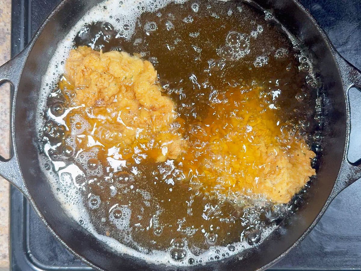 Chicken thighs frying in hot oil in a cast iro Dutch oven.