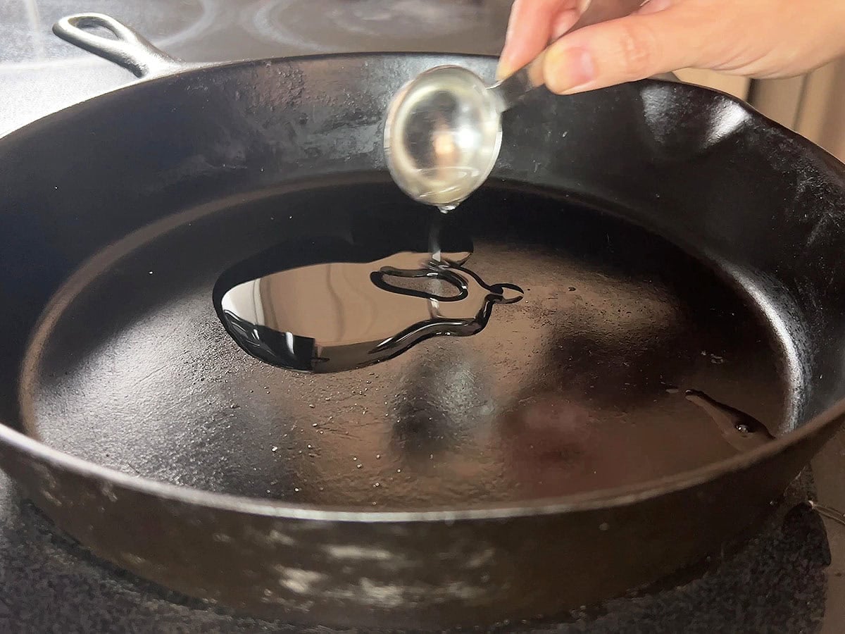 Measuring a tablespoon of oil in a cast iron skillet.