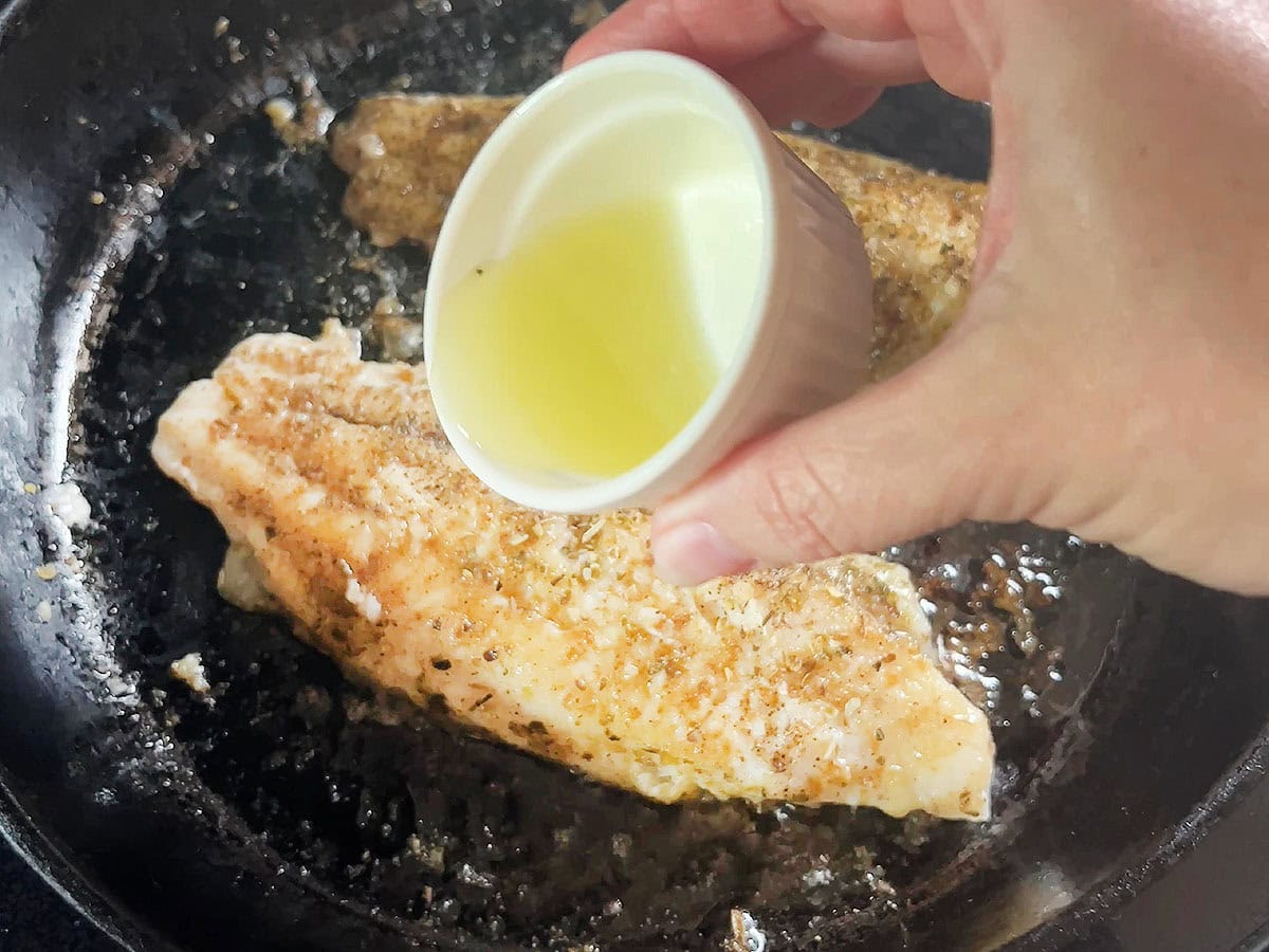 Pouring lime juice over two catfish fillets in a cast iron skillet.