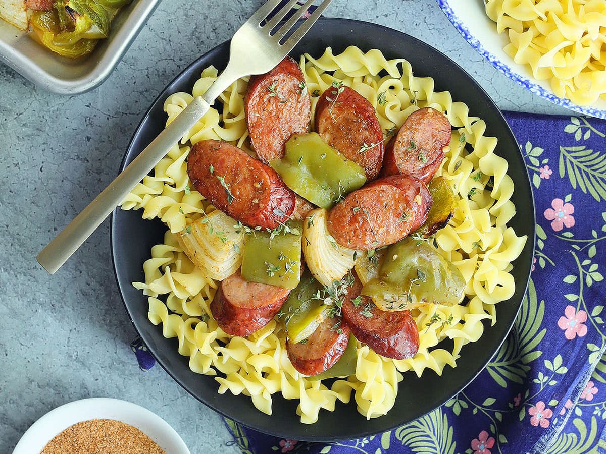 Smoked sausage dinner served over egg noodles in serving bowl.