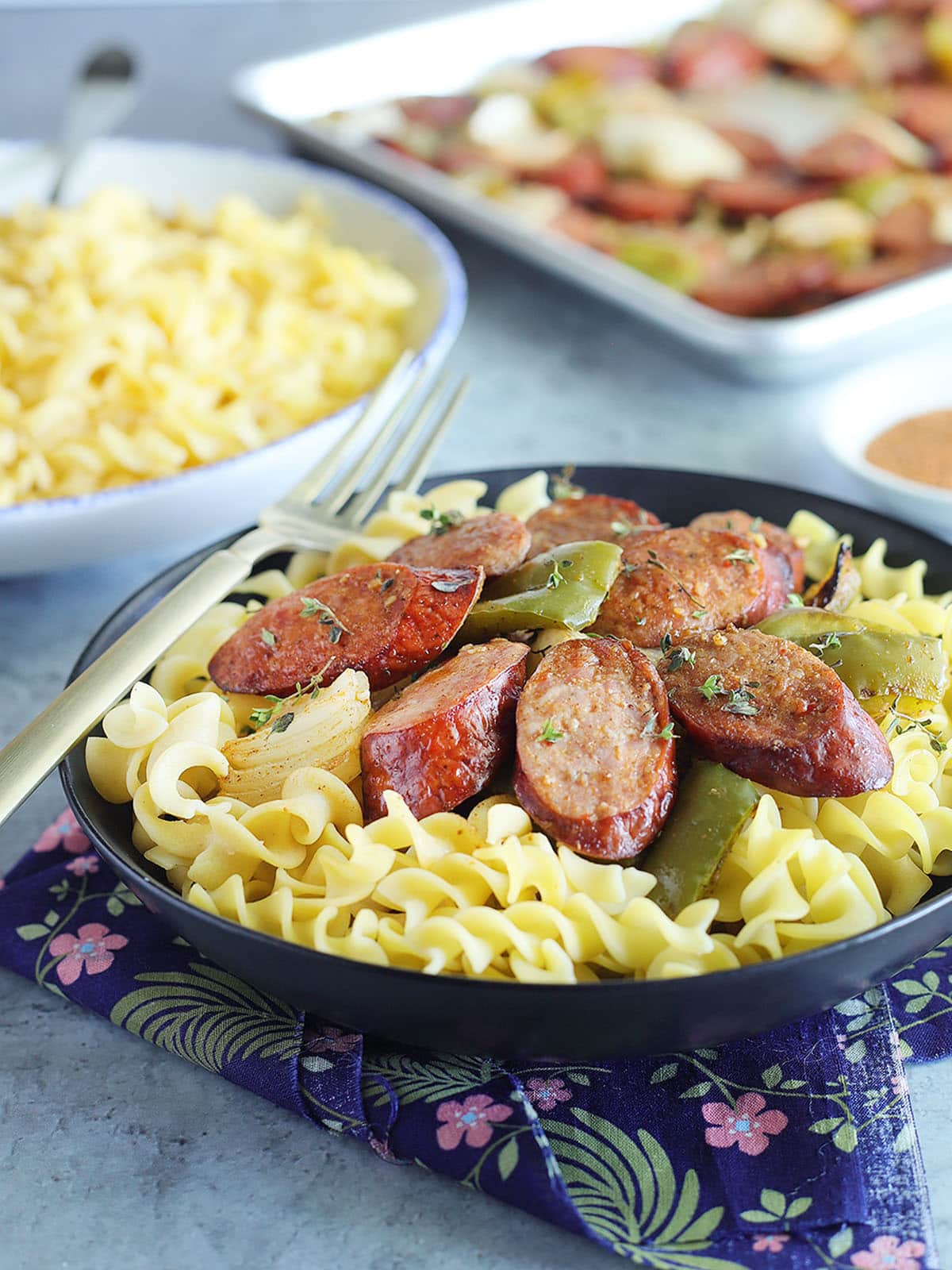 Bell pepper and smoked sausage dinner in a serving dish over buttered egg noodles.