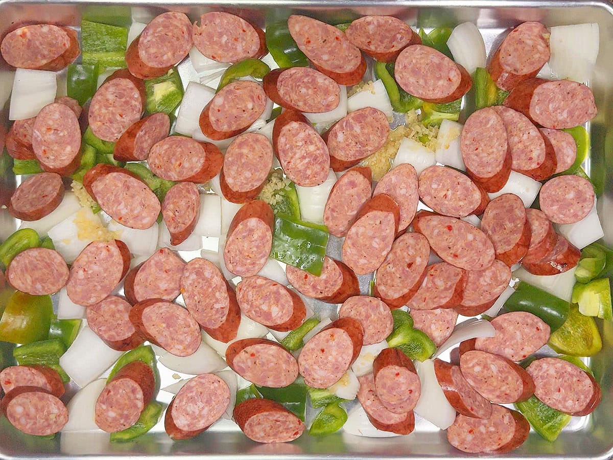 Diced onions, green bell peppers, smoked sausages and minced garlic on a sheet pan.