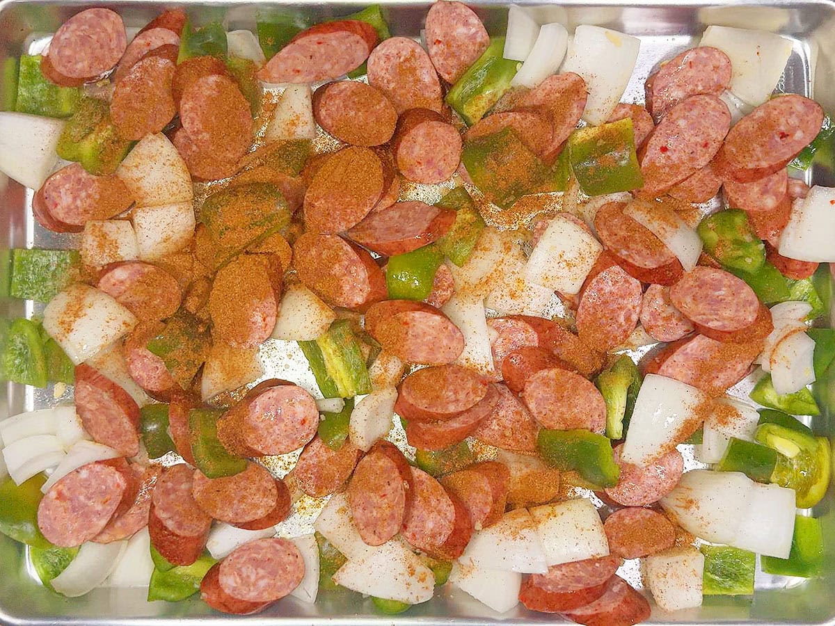 Seasoning the vegetables and smoked sausage with olive oil and Cajun seasoning.