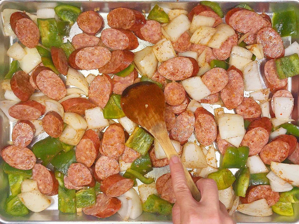 Spreading the seasoned smoked sausage and vegetables into a single layer on a sheet pan.