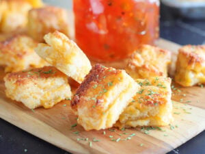 Cheese dreams garnished with dried thyme on a cutting board with a jar of pepper jelly.