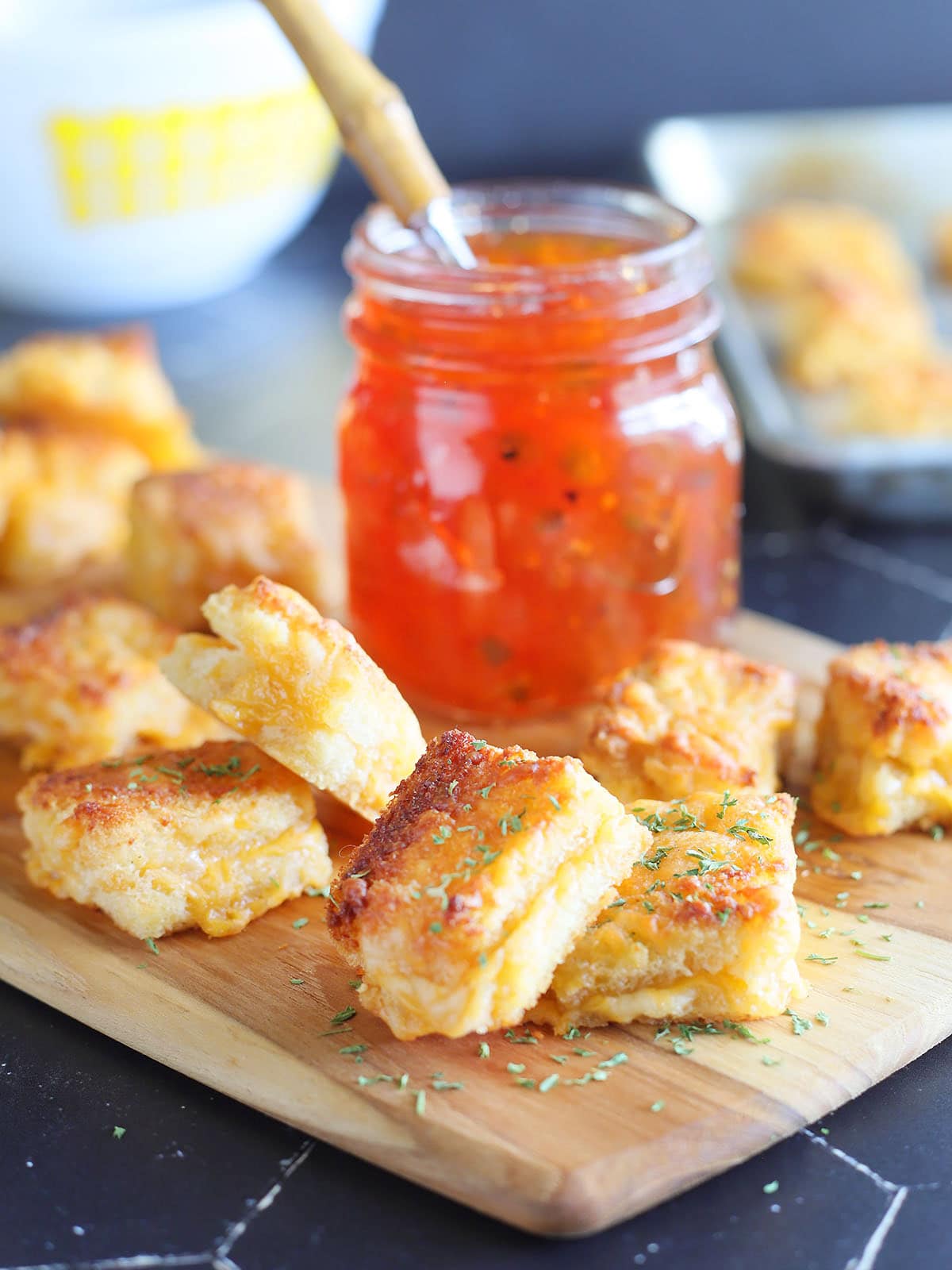 Cheese dreams garnished with dried thyme on a cutting board with a jar of pepper jelly.