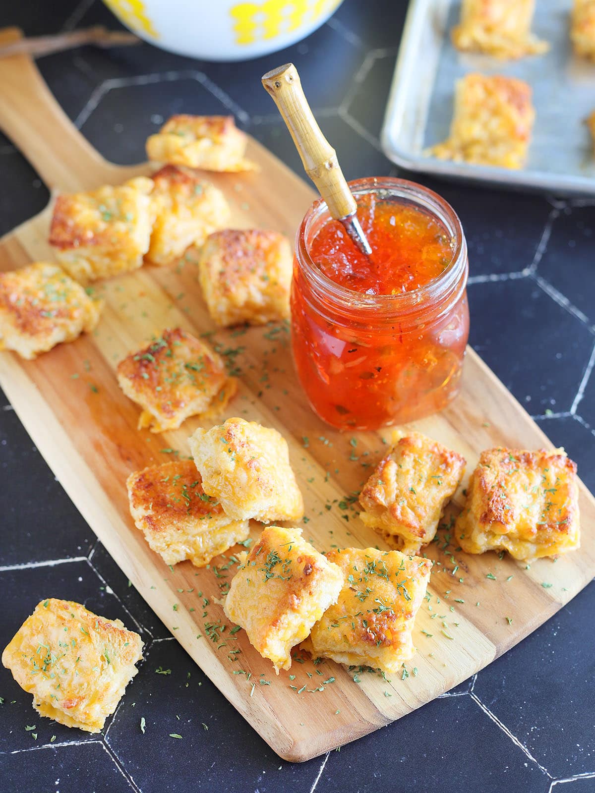 Cheese dreams garnished with dried thyme on a cutting board with a jar of pepper jelly.