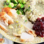 Thanksgiving plate with slices of turkey breast and mashed potatoes covered in giblet gravy with roasted Brussels sprouts and cranberry sauce.