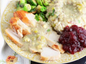 Thanksgiving plate with slices of turkey breast and mashed potatoes covered in giblet gravy with roasted Brussels sprouts and cranberry sauce.