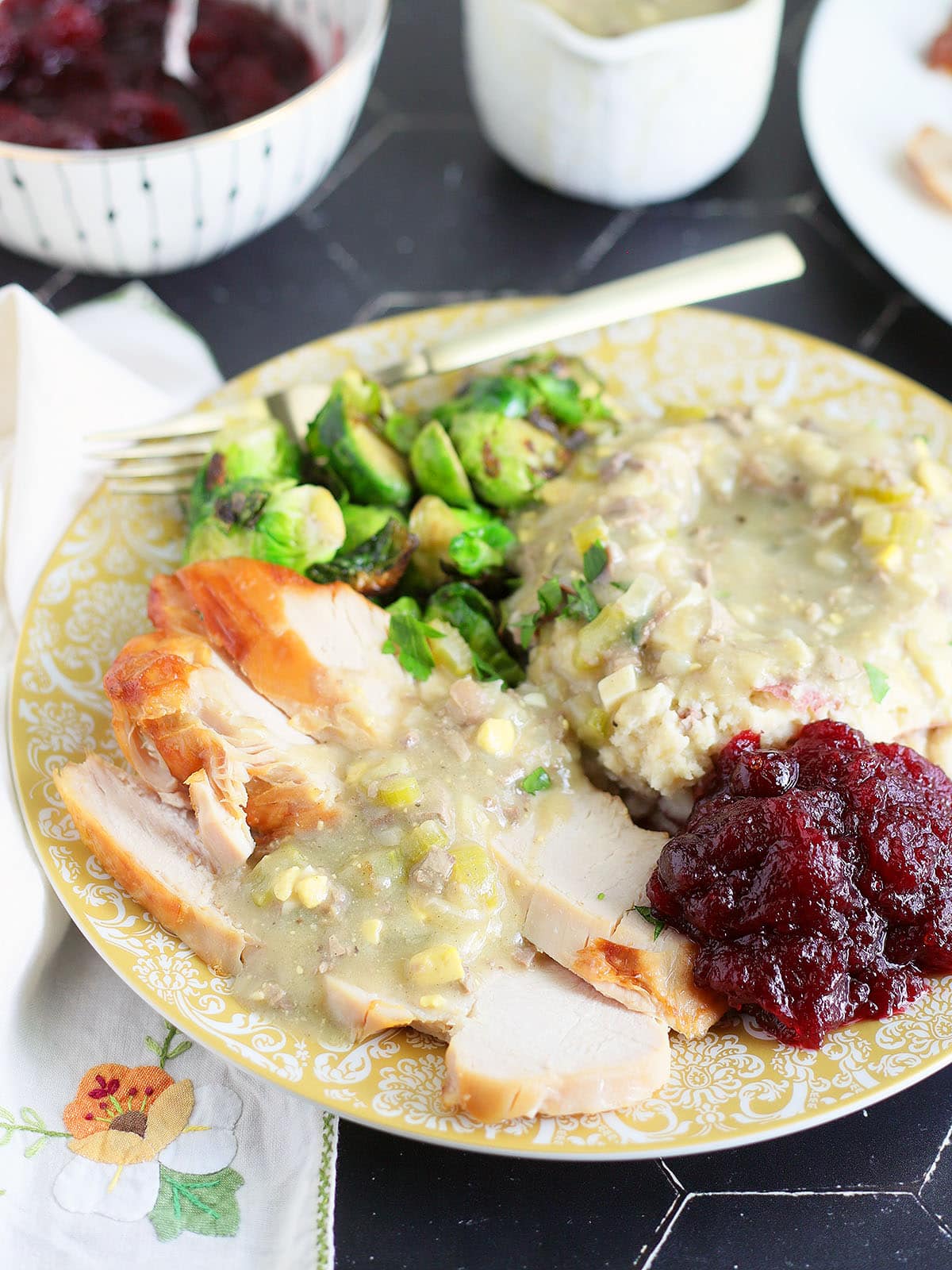 Thanksgiving plate with slices of turkey breast and mashed potatoes covered in giblet gravy with roasted Brussels sprouts and cranberry sauce.