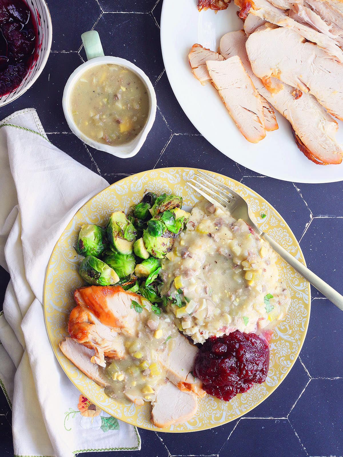 Thanksgiving plate with slices of turkey breast and mashed potatoes covered in giblet gravy with roasted Brussels sprouts and cranberry sauce.
