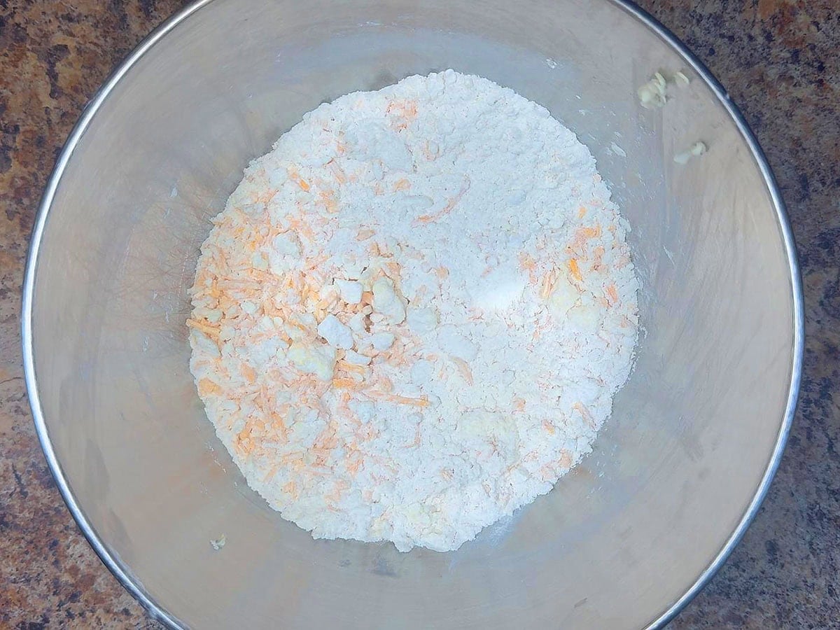 Flour mixture in a large mixing bowl with cold butter, shortening, and shredded cheddar cheese mixed throughout.