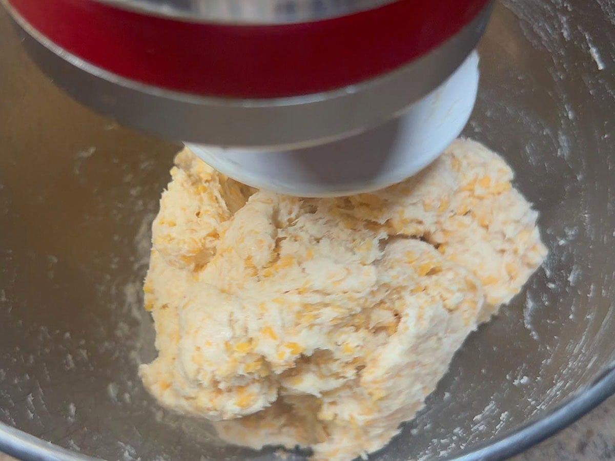 Beating the pie crust dough until it comes together and away from the side of the mixing bowl.