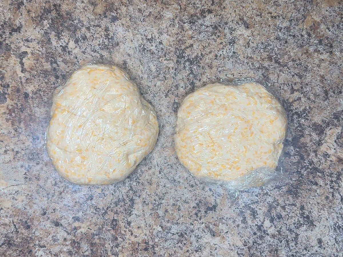 Two pieces of pie crust dough formed into flat disks and wrapped in plastic wrap.