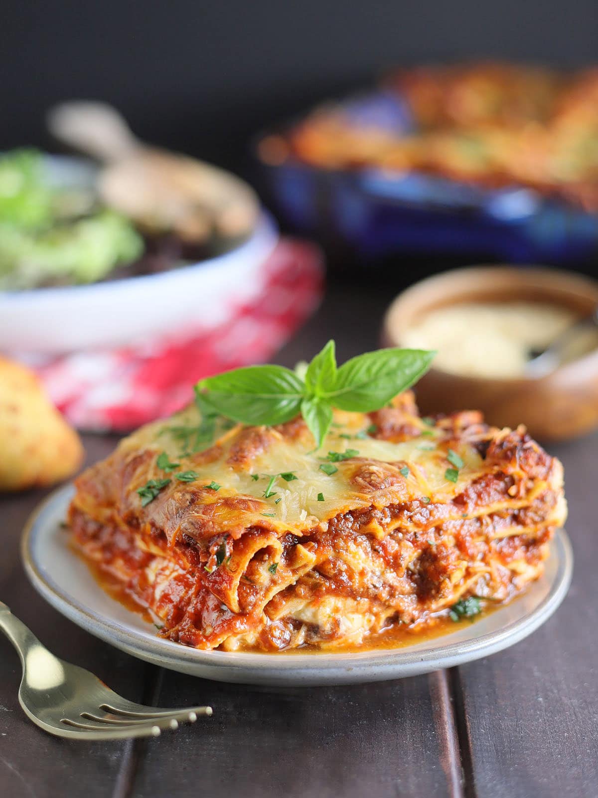 Slice of lasagna on a plate topped with fresh basil leaves.