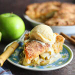 A slice of Granny Smith apple pie with cheddar cheese crust on a plate with a scoop of vanilla ice cream.