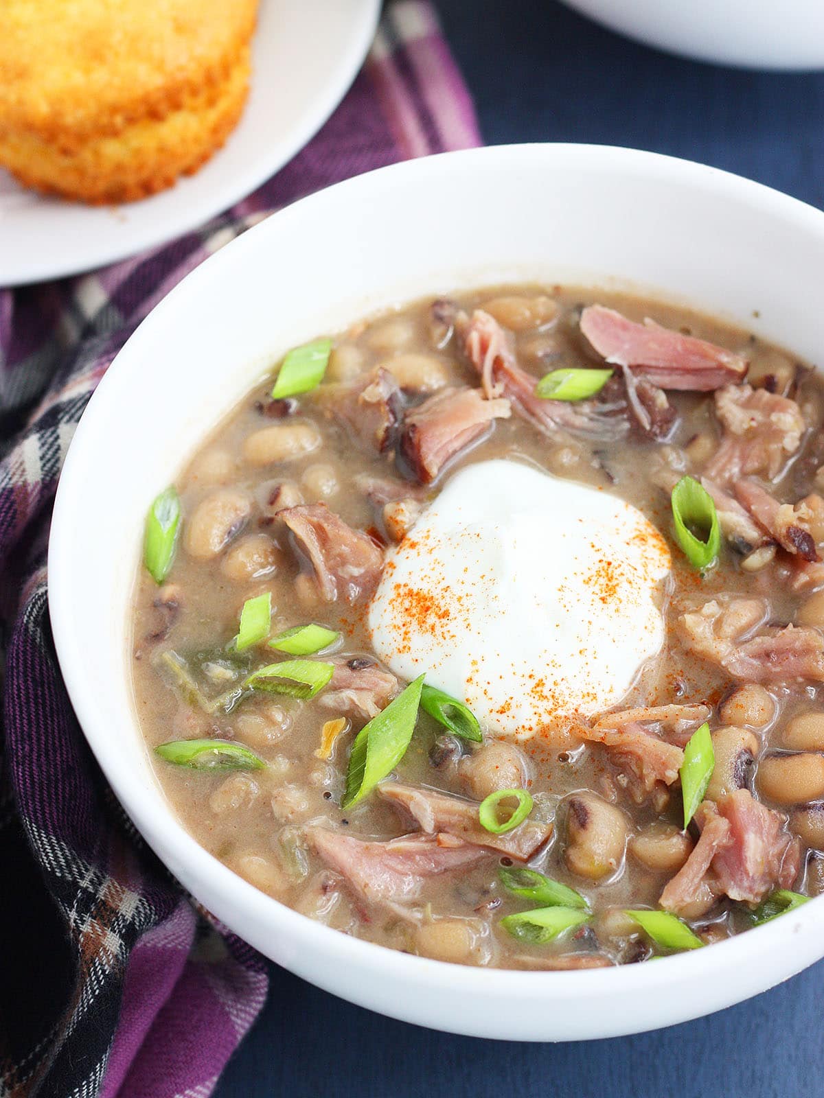 Bowl of black eyed pea soup garnished with a dollop of sour cream and cayenne pepper with a corn muffin on the side.