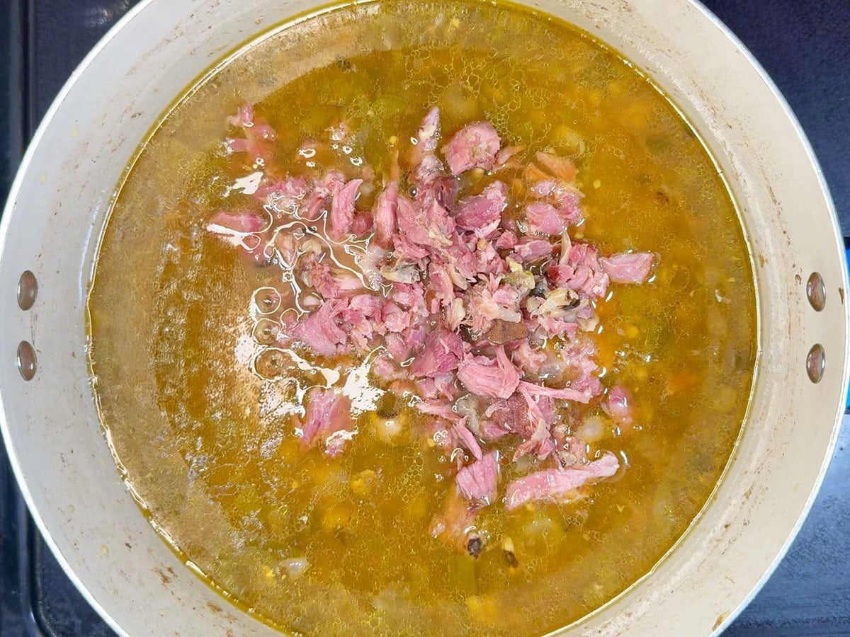 Pile of shredded ham being added to the pot of black eyed pea soup.