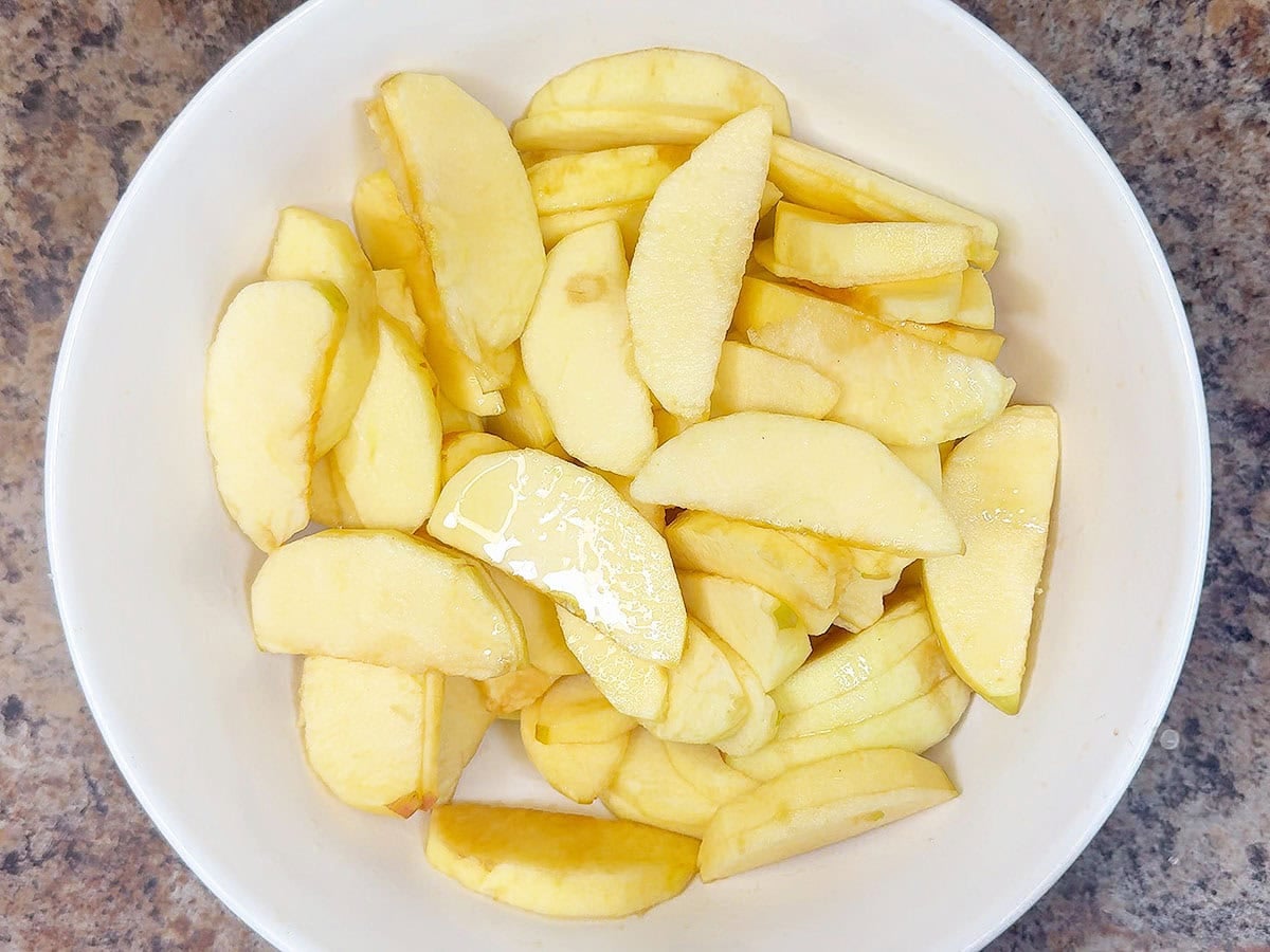 Sliced apples mixed with lemon juice in a mixing bowl.