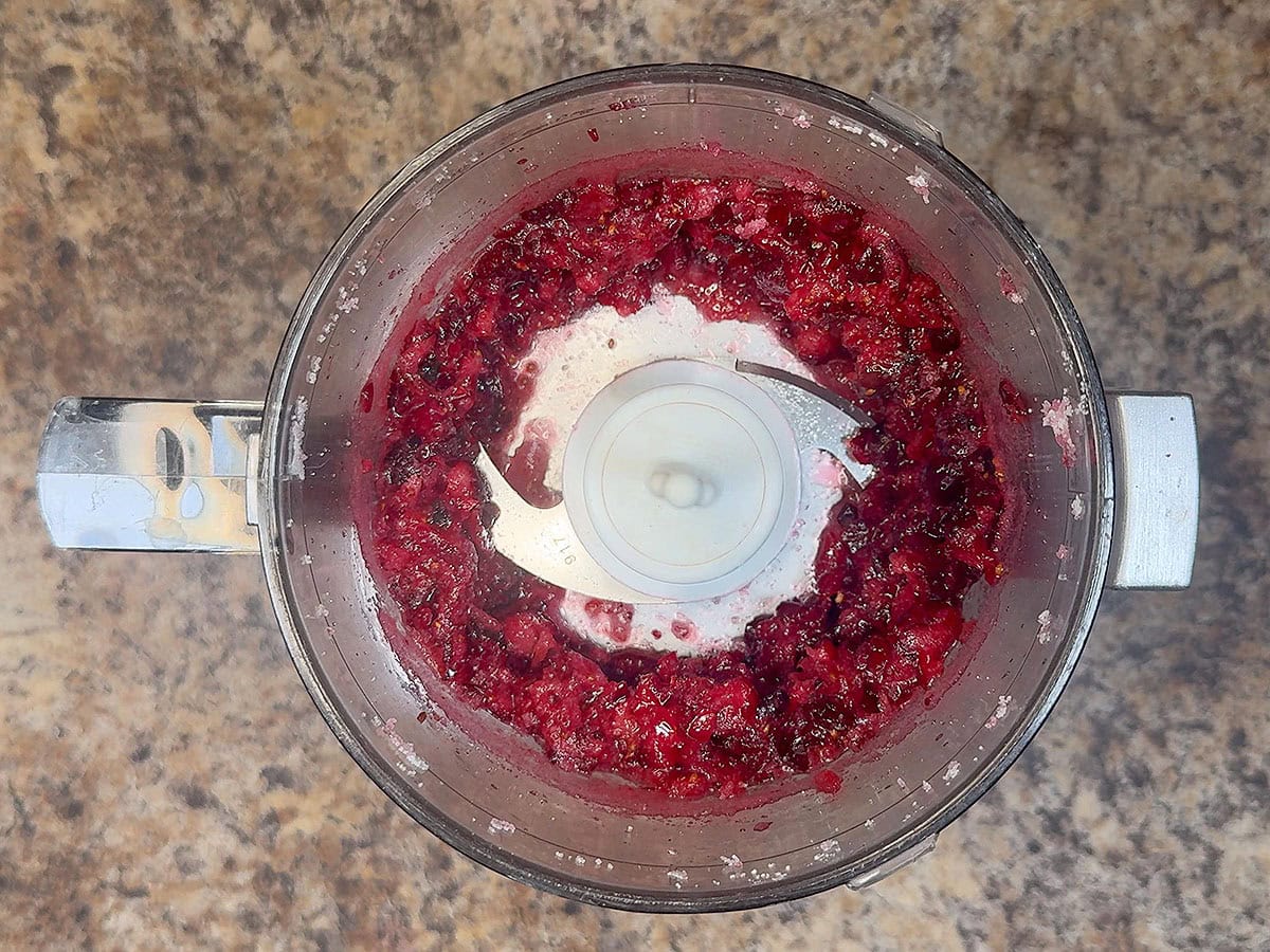 Cranberries chopped with sugar in the bowl of a food processor.