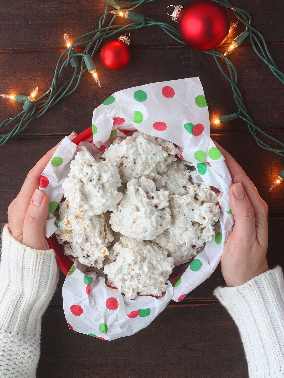 Pair of hands placing an bowl of coconut and cornflake cookies on a holiday table.