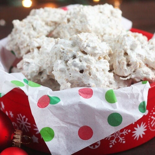 Pile of coconut and cornflake cookies in a red holiday tin lined with Christmas tissue paper.