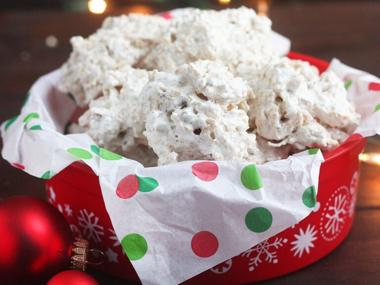 Pile of coconut and cornflake cookies in a red holiday tin lined with Christmas tissue paper.