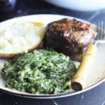 Serving of creamed spinach on a plate with a grilled steak and baked potato.